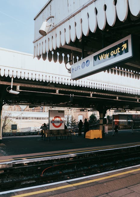 Photograph of the entrance to Camden Town Underground Station, built with red brick and featuring large arched windows. The station sign is prominently displayed in blue with white lettering, reading 